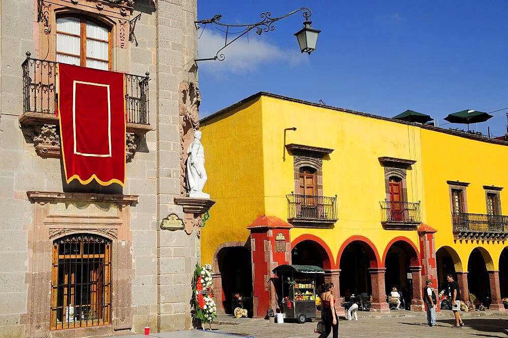 Mexico, Bajio, San Miguel de Allende, El Jardin Part view of Museo Casa de Allende and yellow painted arcades people and fruit juice vendor.