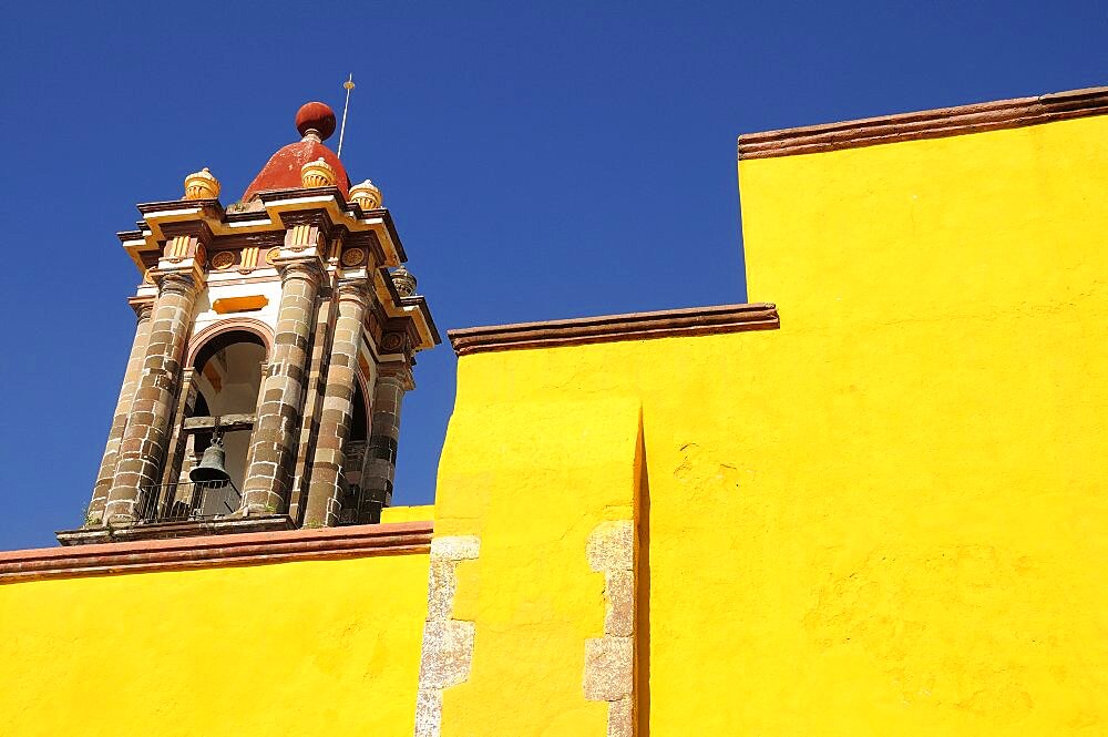 Mexico, Bajio, San Miguel de Allende, Part view of bright yellow exterior wall and church bell tower.