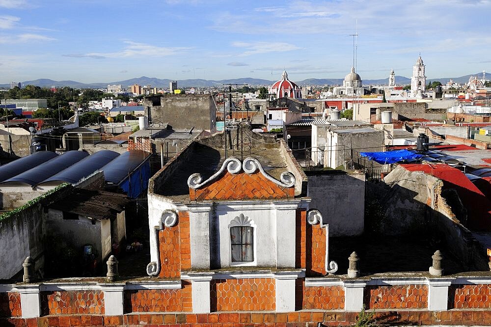 Mexico, Puebla, View across city rooftops with part view of red brick and white building facade in foreground.