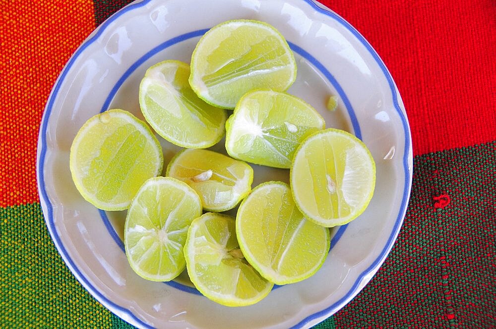 Mexico, Oaxaca, Huatulco, Blue and white bowl with cut halves of limes on red and green woven cloth.