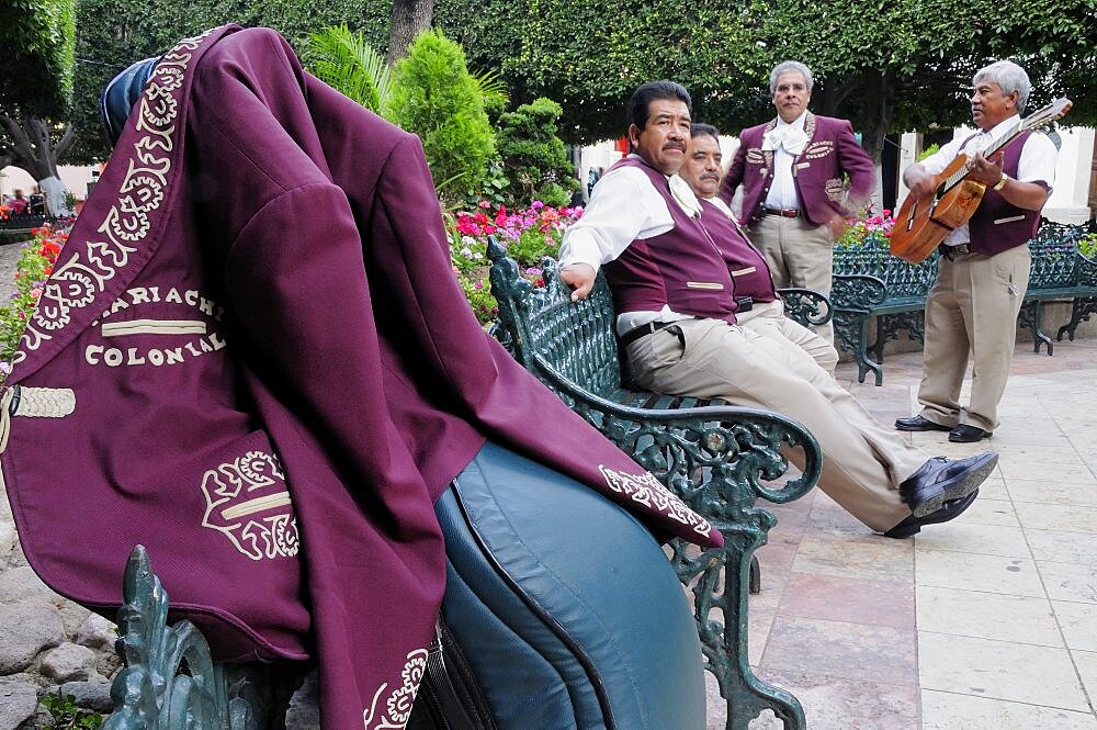 Mexico, Bajio, Guanajuato, Jardin de la Union Mariachi group taking a rest from playing purple jacket hung over music case in foreground.