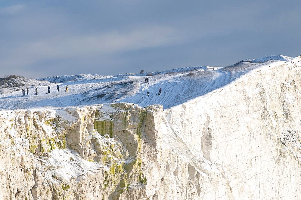 England, East Sussex, Seaford Head, Snow on cliffs with people toboganing.