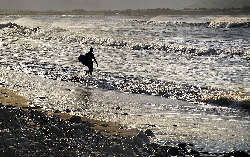 Ireland, County Sligo, Strandhill, Silhouette of surfer with surfboard heading into the sea .