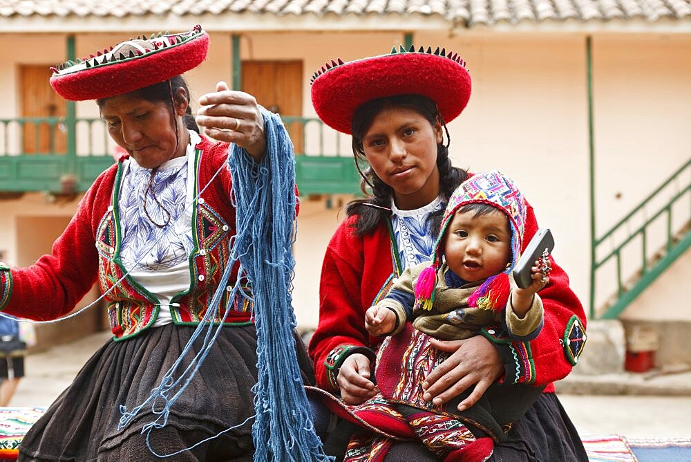 Peru, Indigenous People, Mother and baby in traditional dress with a lady making yarn and infant holding mobile phone.