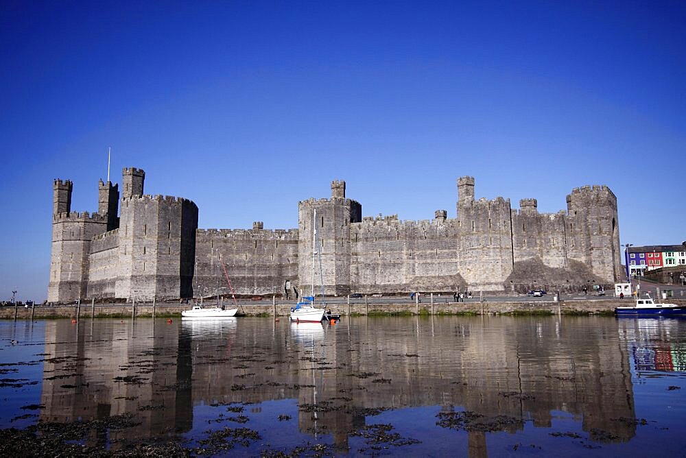 Wales, Gwynedd, Caernarfon, Caernarfon Castle Against Deep Blue Sky Overlooking The River Seiont as the tide comes in Construction Started In 1283 And Prince Charles Held His Investiture At The Castle In 1969. A UNESCO World Heritage Site.