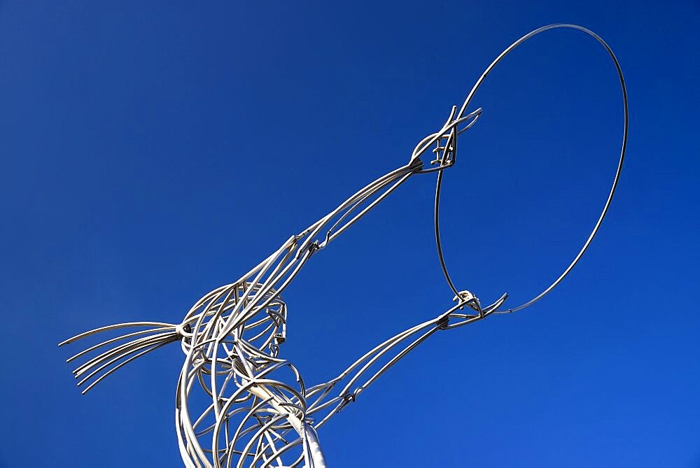 Ireland, North, Belfast, Ring of Thanksgiving sculpture, angular low viewpoint of modern metal sculpture depicting female figure holding up hoop against cloudless blue sky.