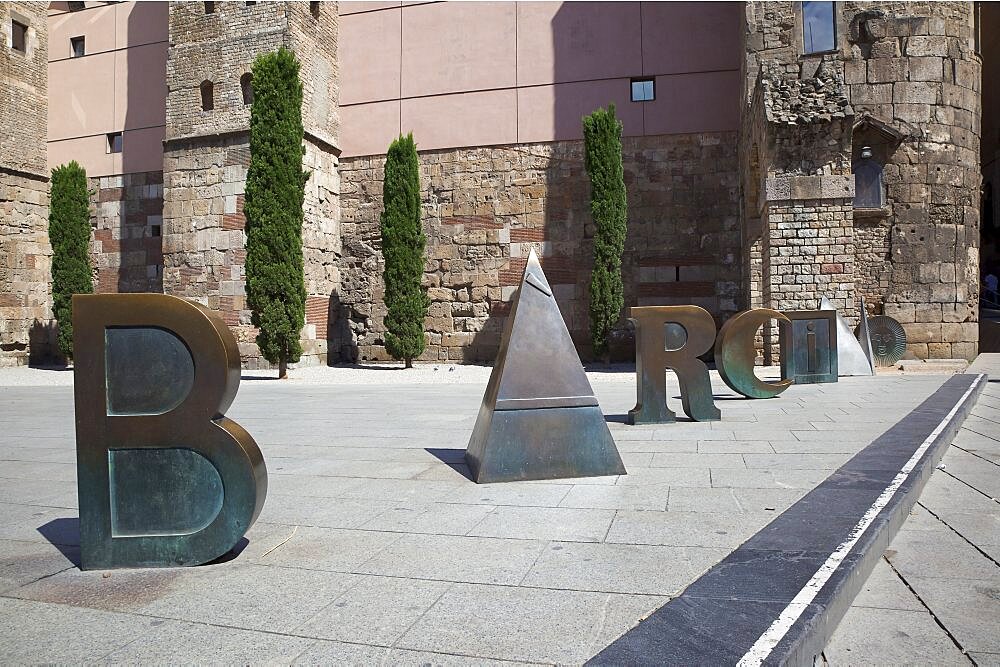 Spain, Catalonia, Barcelona, Scuplture by Joan Brossa in front of Barcelonas Roman wall, where the aqueduct once entered the city and spells out the word Barcino, the Roman name of Barcelona.