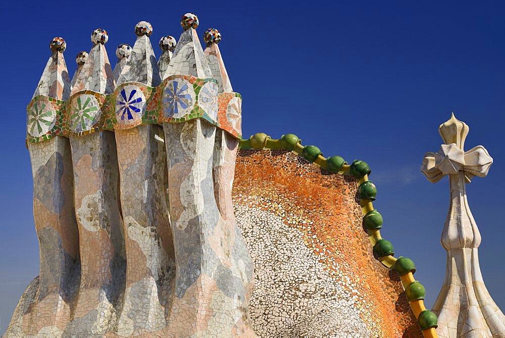 Spain, Catalunya, Barcelona, Antoni Gaudi's Casa Batllo building, colourful chimney pots on the roof terrace with the four armed cross also inclluded.