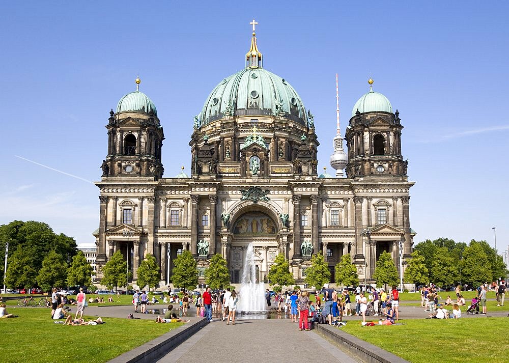 Germany, Berlin, Mitte, Museum Island. Berliner Dom, Berlin Cathedral. people cooling down in a fountain in Lustgarten in front of the church with copper green domes and the Fernsehturm TV Tower beyond.