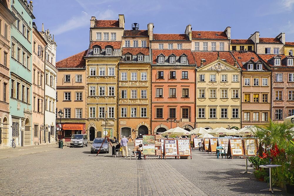 Poland, Warsaw, Stare Miasto or Old Town Square, Colourful facades of buildings on the north side of the square with open air restaurant and artwork on display.