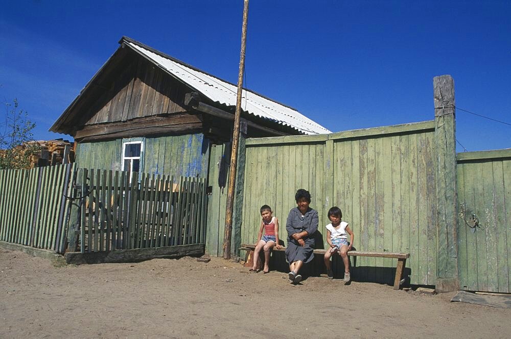 RUSSIA Lake Baikal Buryat woman and children outside painted wooden fence of house.  The Buryat are of Mongolian descent and are the largest ethnic minority group in Siberia.