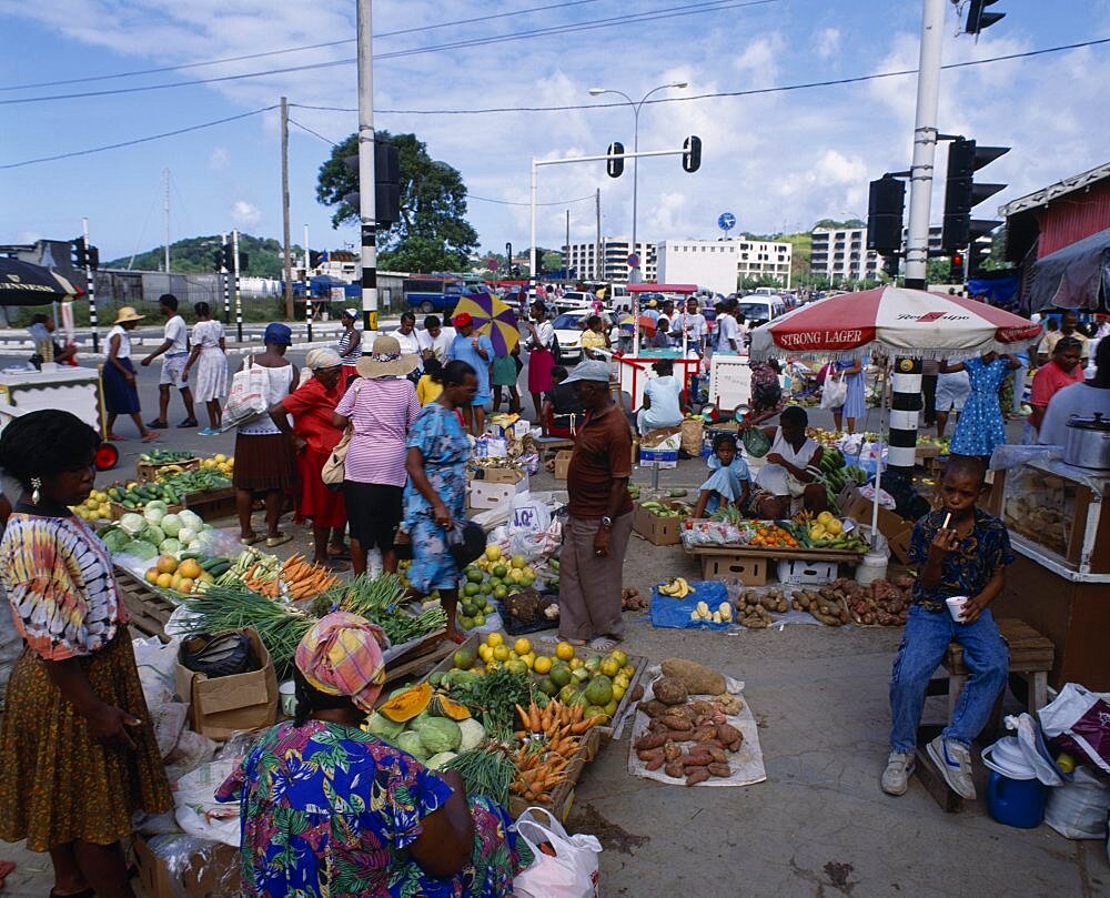 WEST INDIES St Lucia Castries Fruit and  vegetable street market. Pumpkins  carrots  cabbage  yams  spring onions  bananas  oranges near street with traffic lights and ice-cream vendor in background.