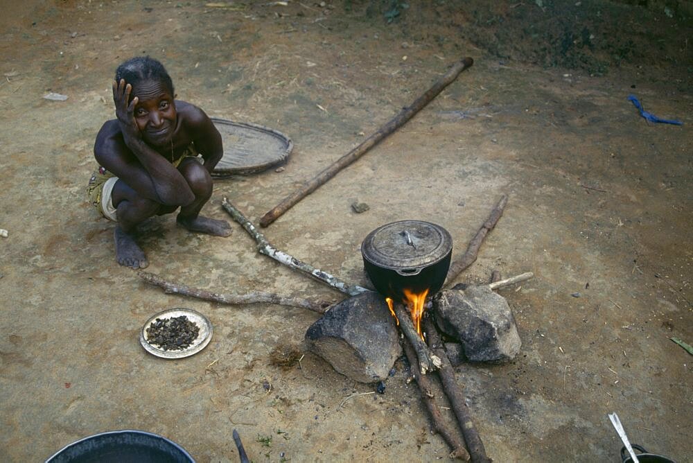 LIBERIA  People Woman cooking on open fire with cooking pot balanced on stones.