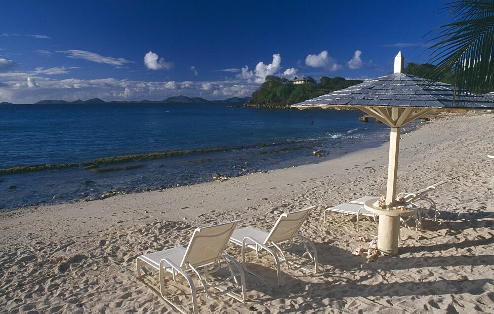 GRENADINES  Mustique Endeavour Bay. Empty sun loungers on sandy beach with Bequia Island seen from across the sea in the distance