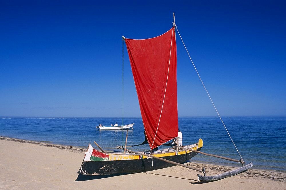 MADAGASCAR  Tulear Ifaty Beach. Pirogue boat with red sail on sandy beach next to the waters edge