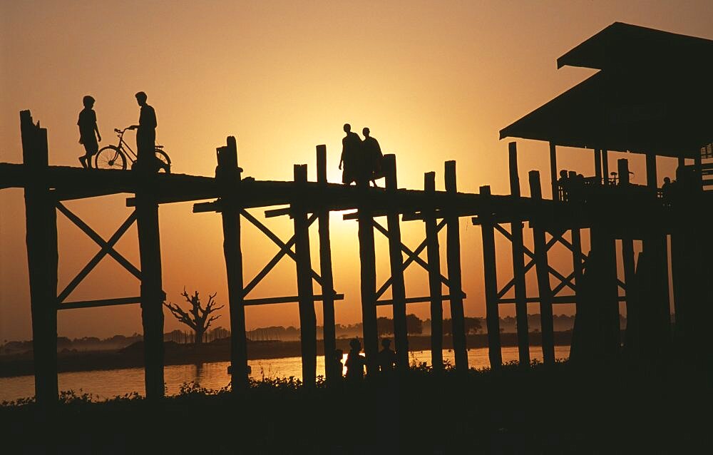 MYANMAR  Amarapura U Bein Bridge near Mandalay at sunset with silhouetted figures of monks  child and cyclist crossing. Burma Myanmar