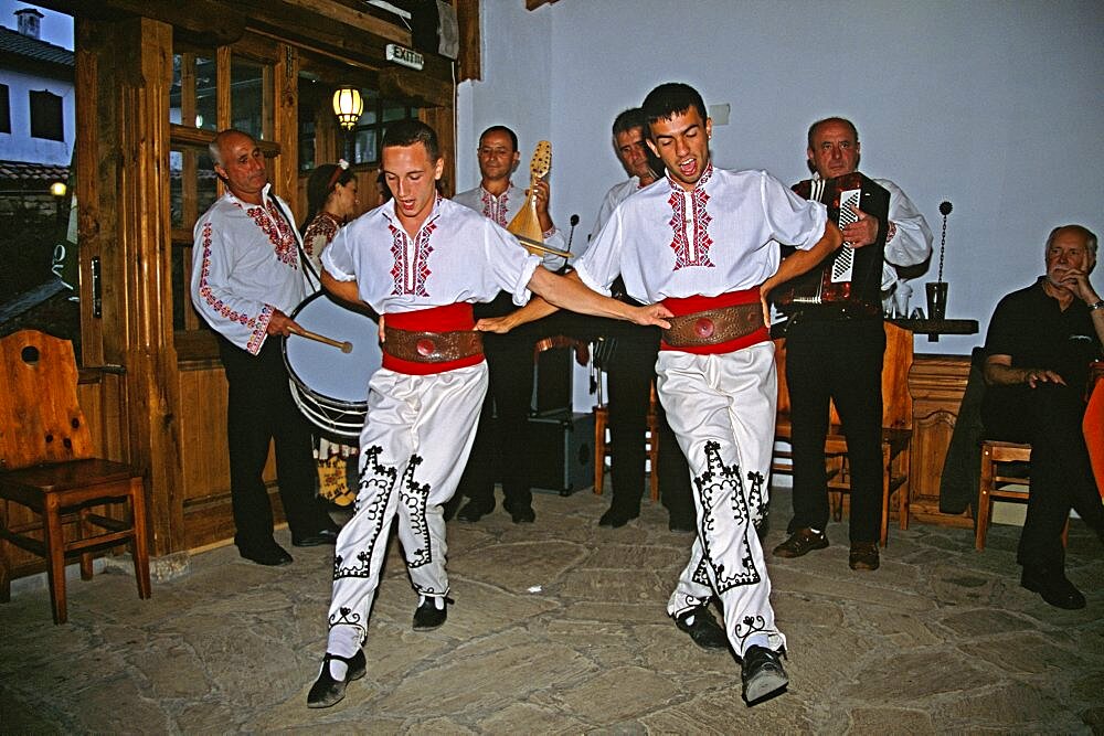 BULGARIA  Arbanassi Male dancers in national costume dancing. Travel Tourism Holiday Vacation Explore Recreation Leisure Sightseeing Tourist Attraction Tour Arbanassi Bulgaria Bulgarian East Eastern Europe European Entertain Entertainer Entertainment Entertaining Folklore Smiling Smile Happy Happiness National Costume Calendar Festival Festive Tradition Traditional Culture Cultural Ethnic Folk Group Man Men Male Gentleman Vivid Vibrant Country Dress Community Village Local Floor Show Dance Dancing Dancer Dancers Restaurant Embroidery Embroidered Sewing Sewn Sew Clothes Clothing Garments Garment Adorn Adornment Smart Fashion Fashionable Wear Wearing Worn Detail Detailed Extrovert Activity Active Pattern Patterned Drum Drummer Music Musical Musician Band Contented Eastern Europe