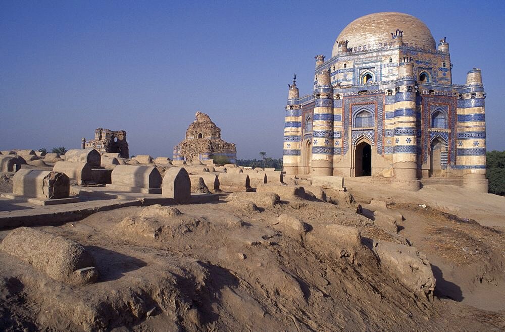 Tomb of Bibi Jawindi with domed roof and two similar crumbling buildings with dusty graveyard in the foreground, Uch Sharif, Pakistan