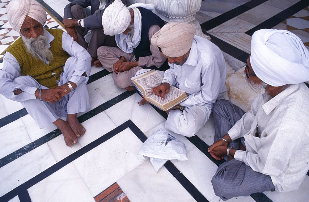 Group of Sikh men sitting on black and white marble floor of Golden Temple complex to read holy book, Amritsar, Punjab, India