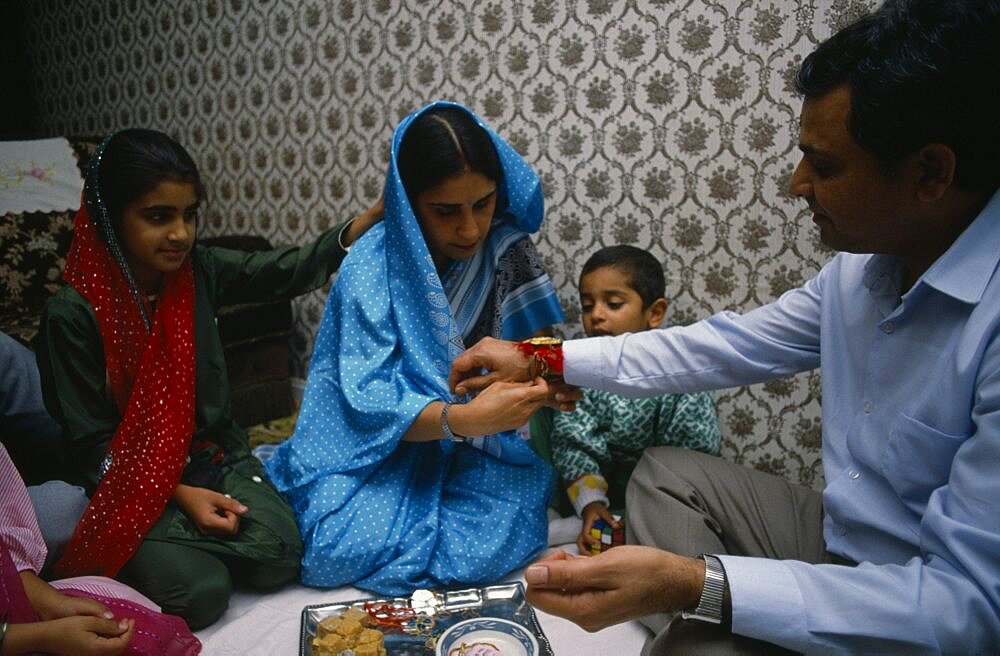 Woman tying thread on wrist of man during the Sacred Thread ceremony, The Hindu male rite of passage ceremony, England, United Kingdom