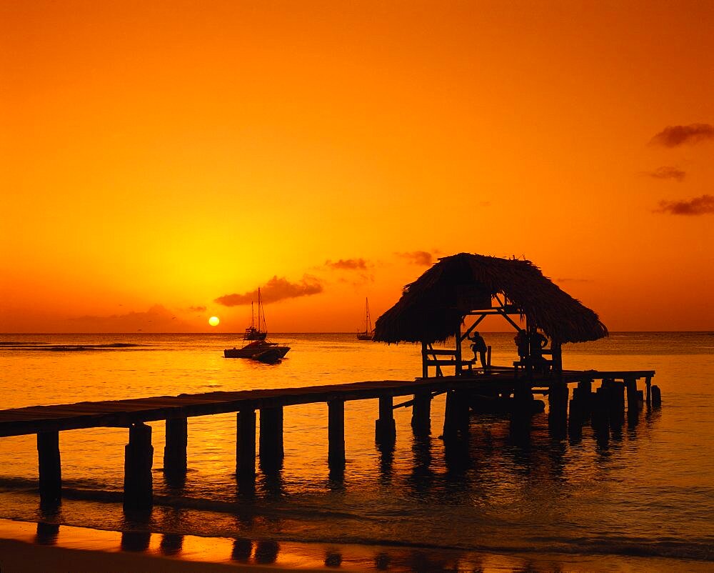 WEST INDIES Tobago Pigeon Point Wooden jet and boat silhouetted at sunset.