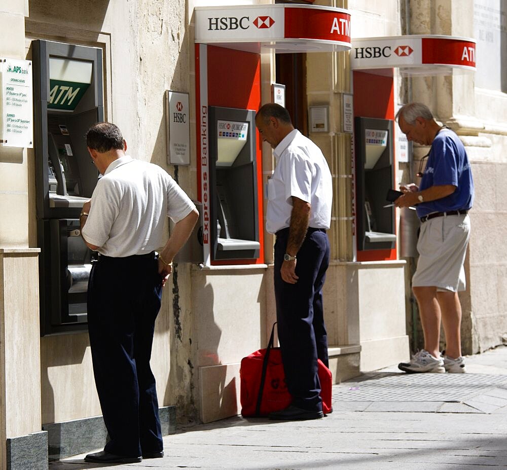 Three men using separate ATM cash machines on Republic Street, Valletta, Malta