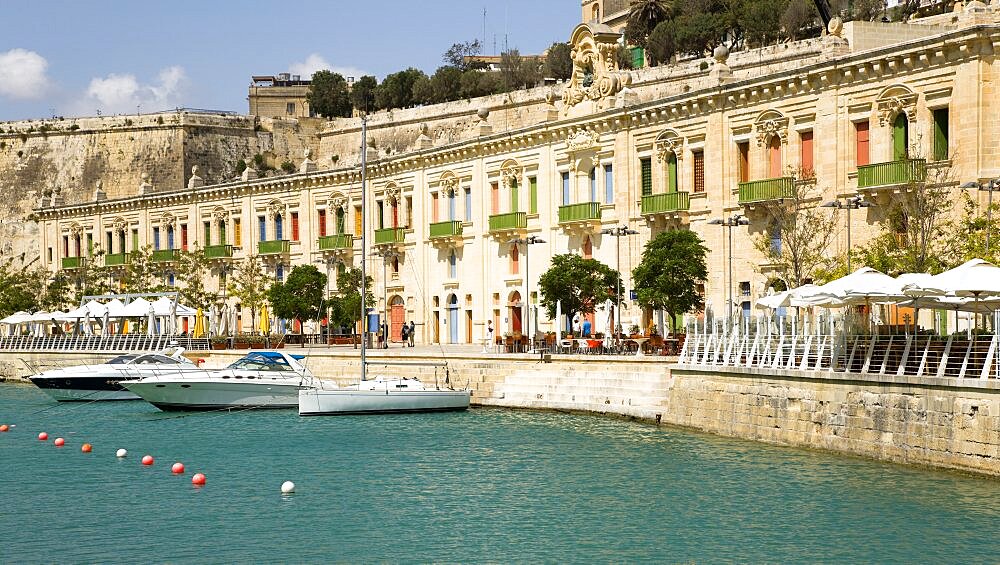 The waterfront redevelopment of old Baroque Pinto wharehouses below the bastion walls of Floriana beside the cruise ship terminal with boats moored alongside, Valletta, Malta