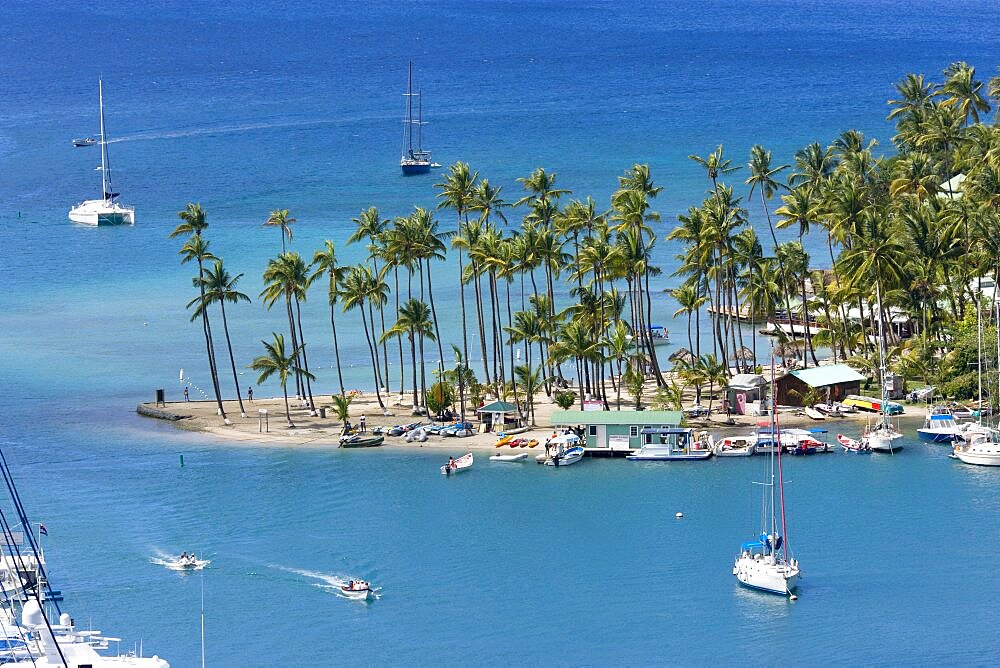 Marigot Bay Yachts at anchor beyond the small coconut palm tree lined beach of the Marigot Beach Club sitting at the entrance, Castries, St Lucia