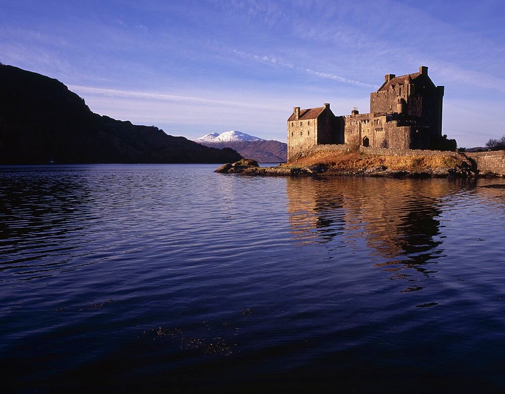 Eilean Donan Castle, View of restored castle reflected in Loch Duich and snow covered Beinin na Caillich on the Isle of Skye beyond, Loch Duich, North West Highlands, Scotland, United Kingdom