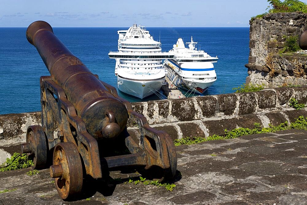 An old cannon pointing out to sea at Fort George with the Caribbean Princess and Aida Aura cruise ships moored below at the cruise ship terminal, St. Georges, Grenada, West Indies, Caribbean, Central America