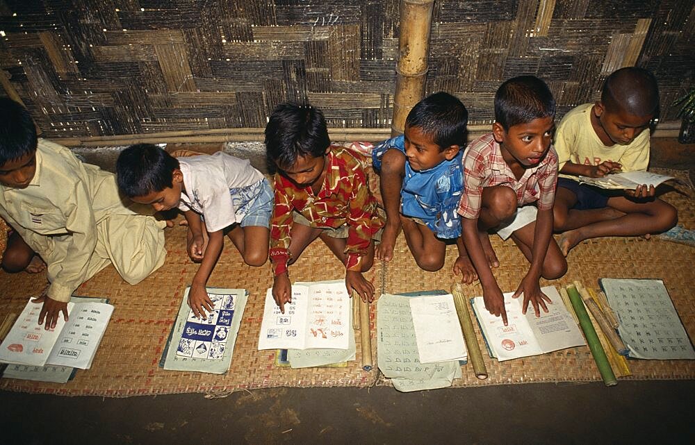 Schoolboys sitting on mats on floor of village school learning to read, Bangladesh, Asia