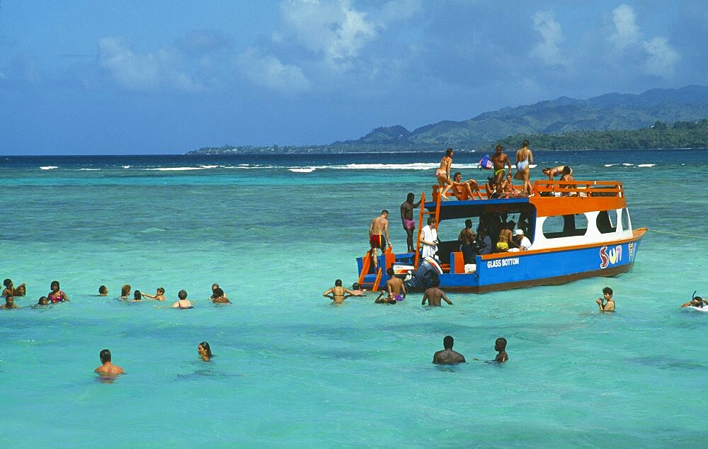 WEST INDIES Tobago Buccoo Reef The Nylon Pool with tourists swimming or standing in shallow water by crowded glass bottom boat