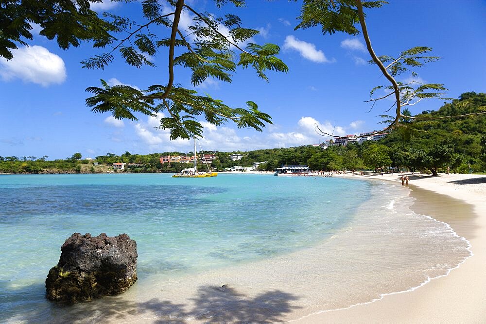 Gentle waves on BBC Beach in Morne Rouge Bay with tourists in the sea on the beach and aboard their tour catamaran in the aquamarine water, Caribbean