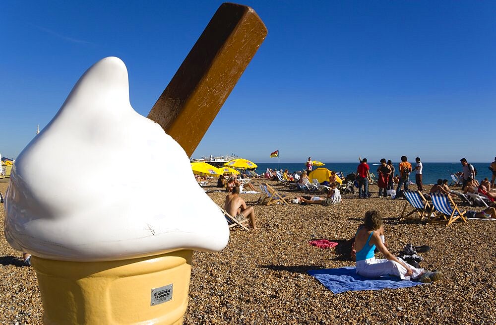 England, East Sussex, Brighton, People sunbathing on the pebble shingle beach with a giant fibreglass model of an ice cream cone in the foreground.