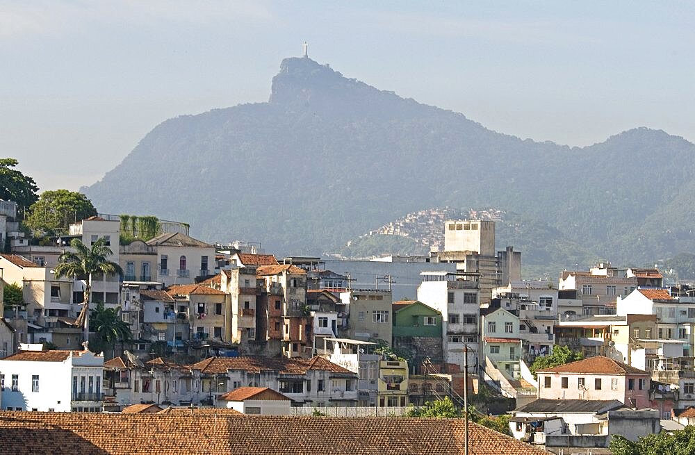 BRAZIL Rio de Janeiro Rooftops of Saude neighbourhood with a hillside favela or slum and the statue of Christ the Redeemer atop Corcovada mountain traditional tile roofs and palm trees