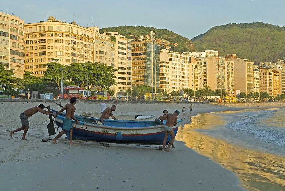 BRAZIL Rio de Janeiro Launching a fishing boat at Copacabana beach at daybreak, fishermen and a few early-morning walkers on the beach, soft sunlight on the hotel facades