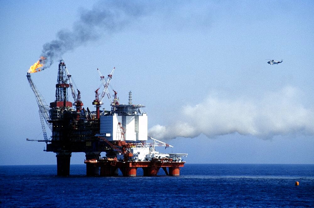 INDUSTRY Factory Oil Rig Worker in a hard hat standing on the deck watching flames from burning off gas over the North sea