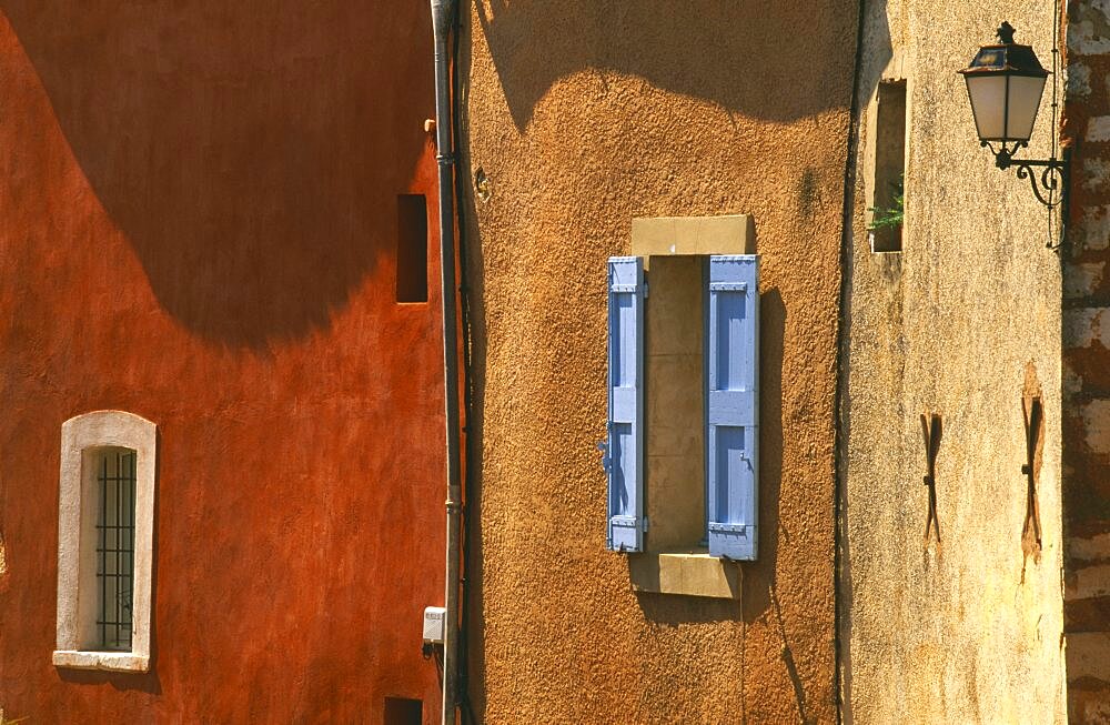 FRANCE Provence-Cote d Azur Vaucluse Roussillon.  Architectural detail of ochre and terracotta coloured walls with blue window shutter and wall lamp.