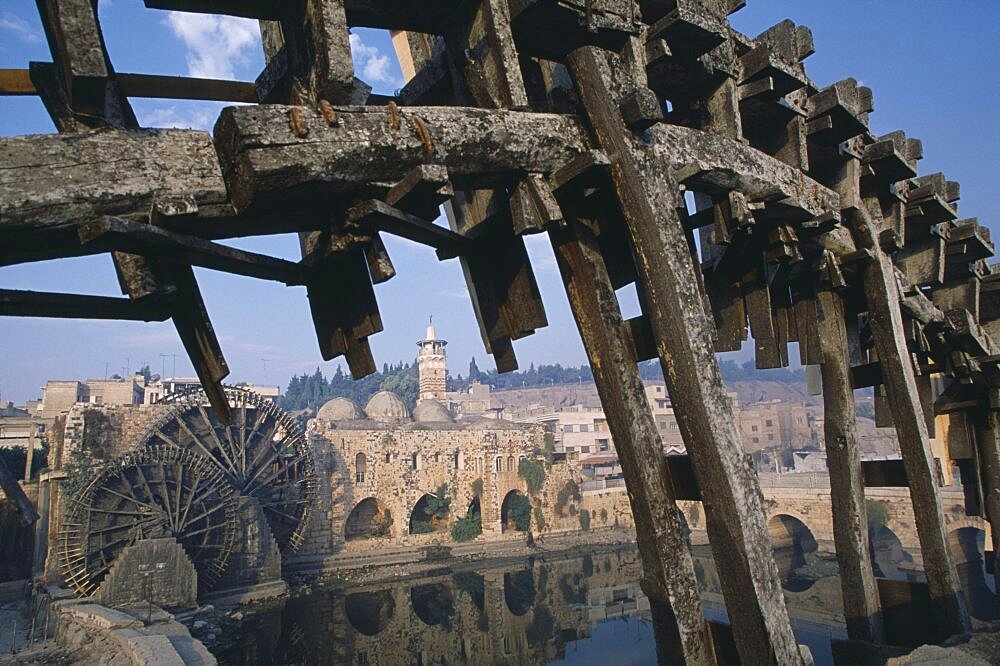 SYRIA Central Hama Wooden norias or waterwheels on the Orontes river.  Part view of wheel section in the foreground framing the Al-Nuri Mosque dating from 1172 and built of limestone and basalt.