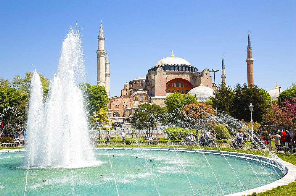 Sultanahmet Haghia Sophia with dome and minarets beyond the water fountain in the gardens with sightseeing tourists, Istanbul, Turkey