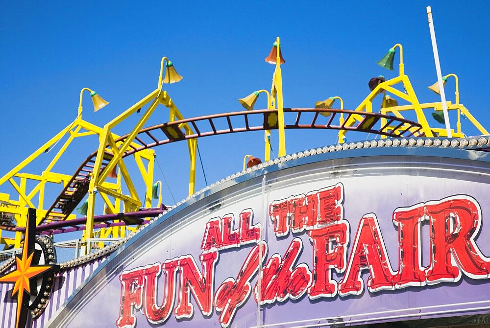 England, Lincolnshire, Skegness, Facade of amusement arcade with rollercoaster behind in clear blue sky.