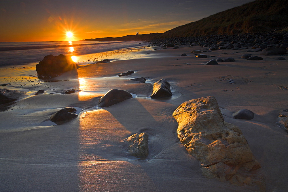 Golden early morning sunshine lights up the sandstone boulders on Dunstanburgh beach, Northumberland, England, United Kingdom, Europe