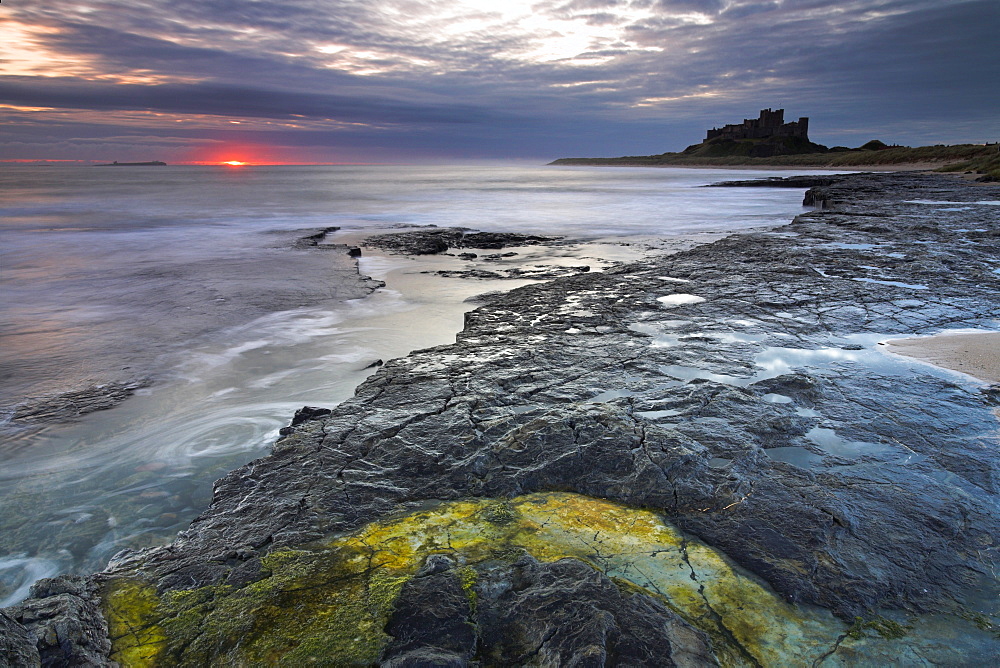 The first glow of sunrise over the sea beside Bamburgh Castle, Bamburgh, Northumberland, England, United Kingdom, Europe