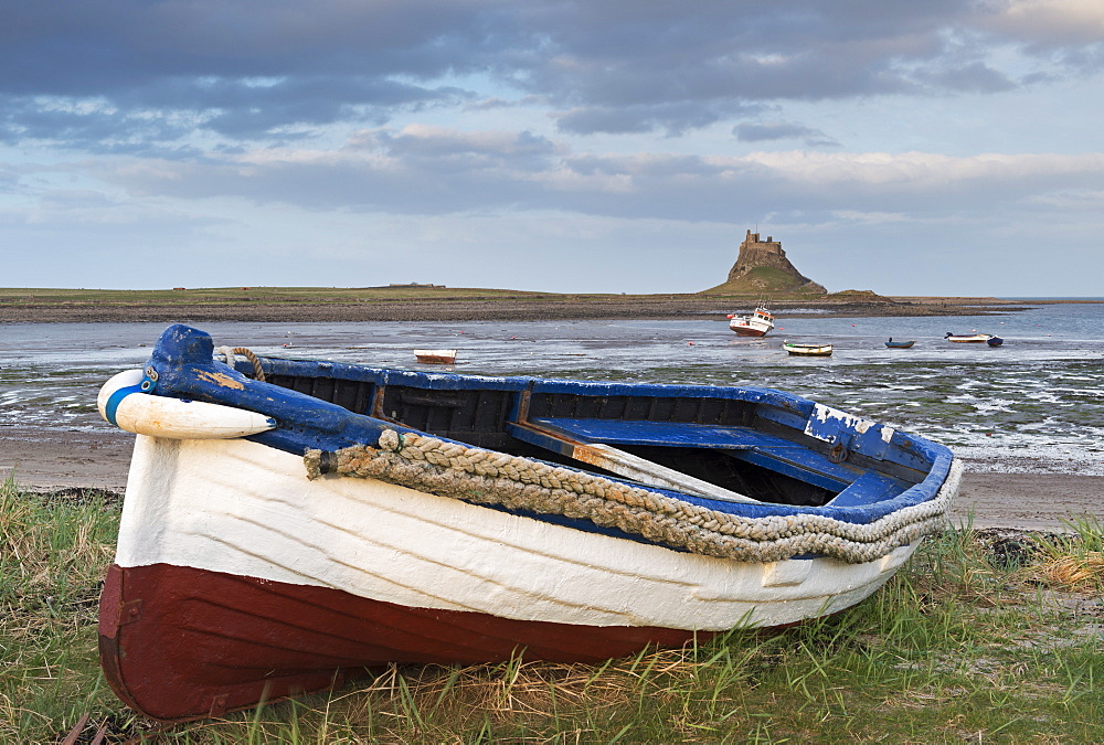 Fishing boat pulled onto the shore at Holy Island, looking towards the castle, Lindisfarne, Northumberland, England, United Kingdom, Europe 