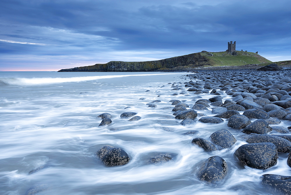 The ruins of Dunstanburgh Castle overlooking the boulder strewn shores of Embleton Bay, Northumberland, England, United Kingdom, Europe 