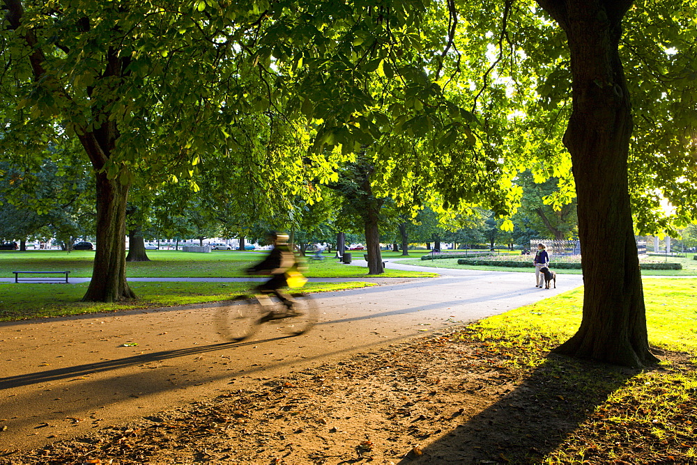 Cyclist and dog walker in Watts Park, Southampton City Centre, Hampshire, England, United Kingdom, Europe