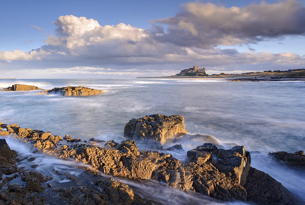 Looking across rocky ledges to Bamburgh Castle, Northumberland, England, United Kingdom, Europe