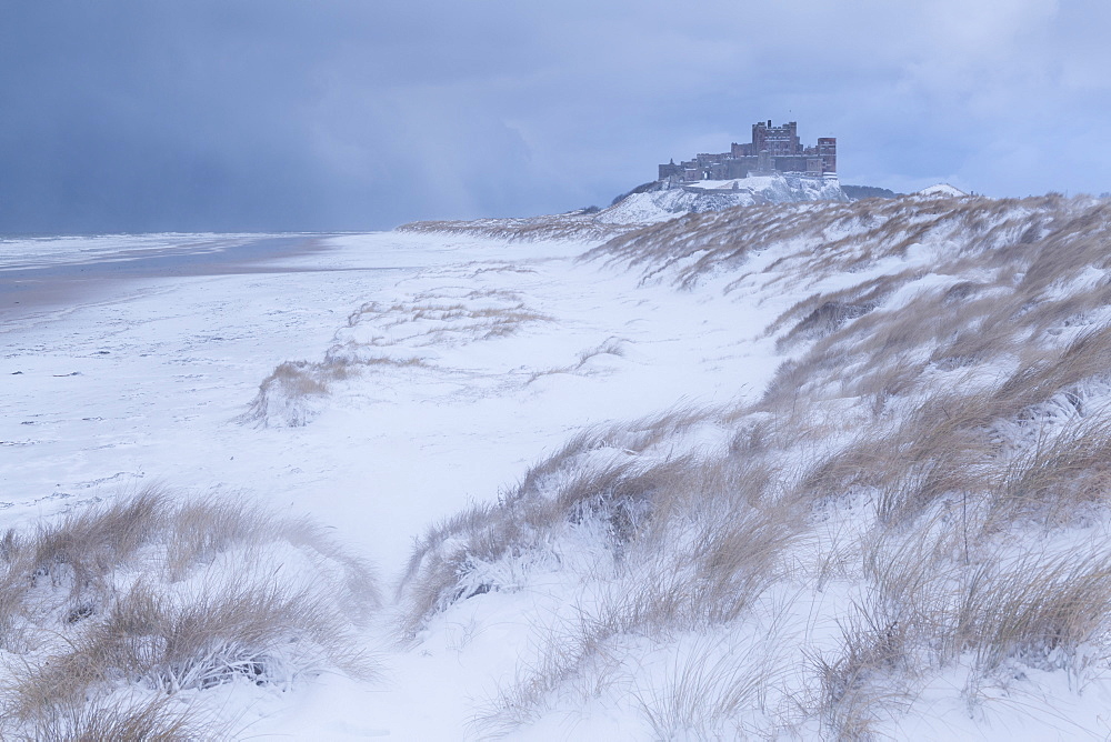 Snow covered beach and sand dunes by Bamburgh Castle in winter, Northumberland, England, United Kingdom, Europe