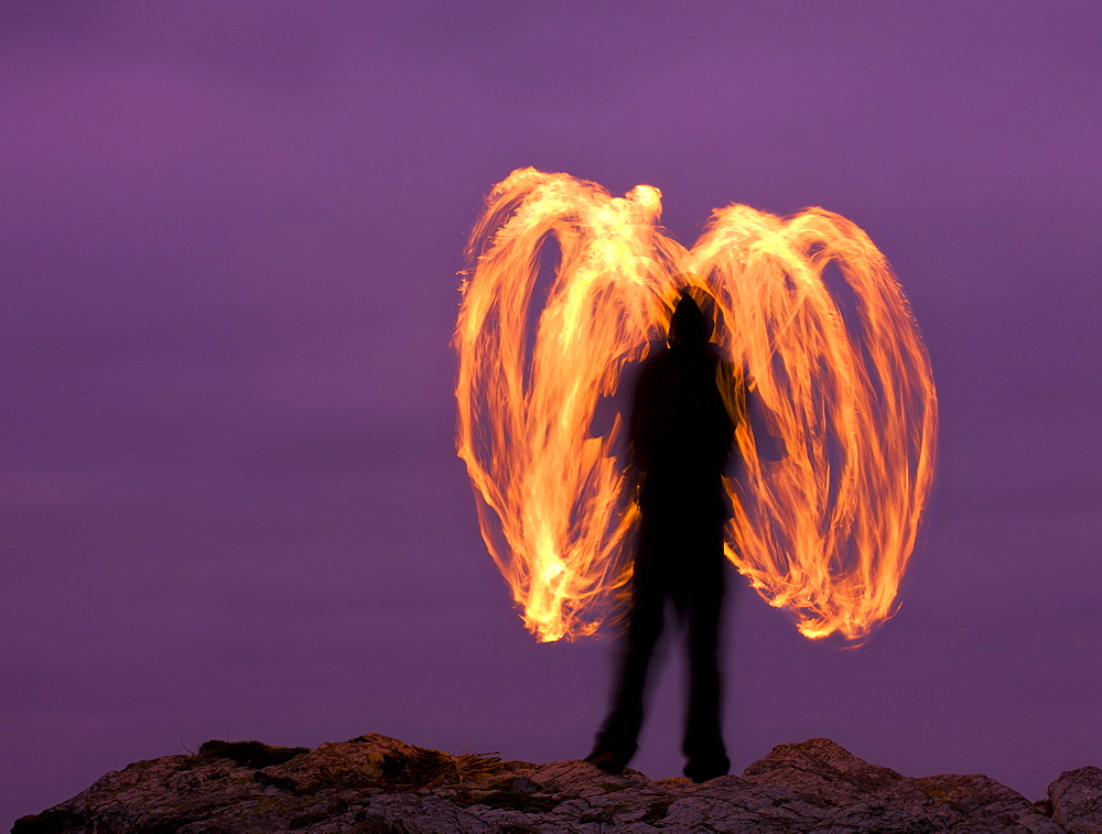 Man fire spinning (Fire Poi) on Cornish clifftops, Godrevy, Cornwall, England, United Kingdom, Europe