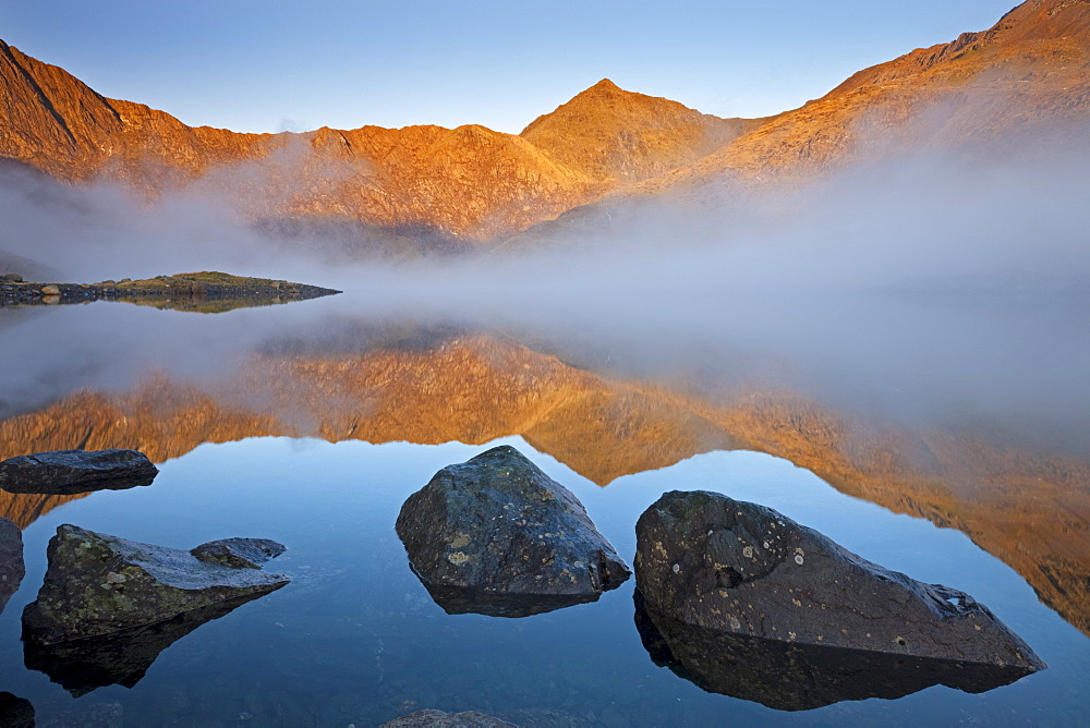 Early morning sunlight illuminates Snowdon from the shores of a misty Llyn Llydaw, Snowdonia National Park, Gwynedd, North Wales, Wales, United Kingdom, Europe